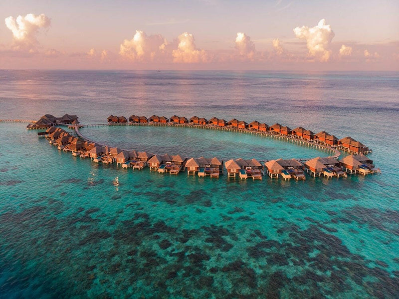Coco Bodu Hithi from the air, a curving loop of thatched water villas above the reef