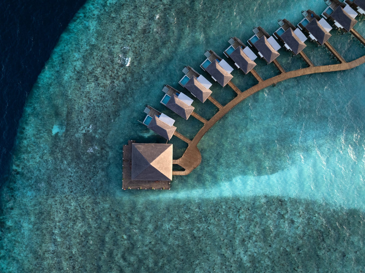 The overwater villas at dusitD2 Feydhoo Maldives seen from overhead, above the reef.