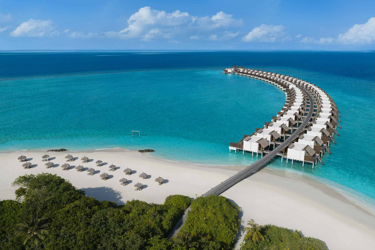 Emerald Maldives Resort & Spa from the air, parasols along the beach and overwater villas curving away