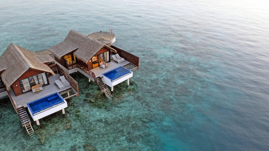 Water villas at Grand Park Kodhipparu standing over the reef edge, each with a blue plunge pool on its deck