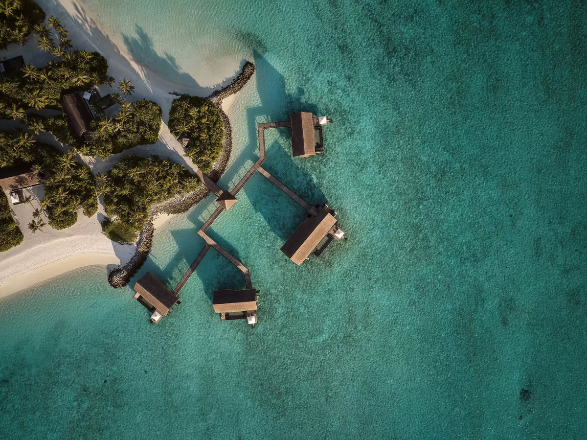 One&Only Reethi Rah from the air, overwater villas branching off timber walkways over the shallows