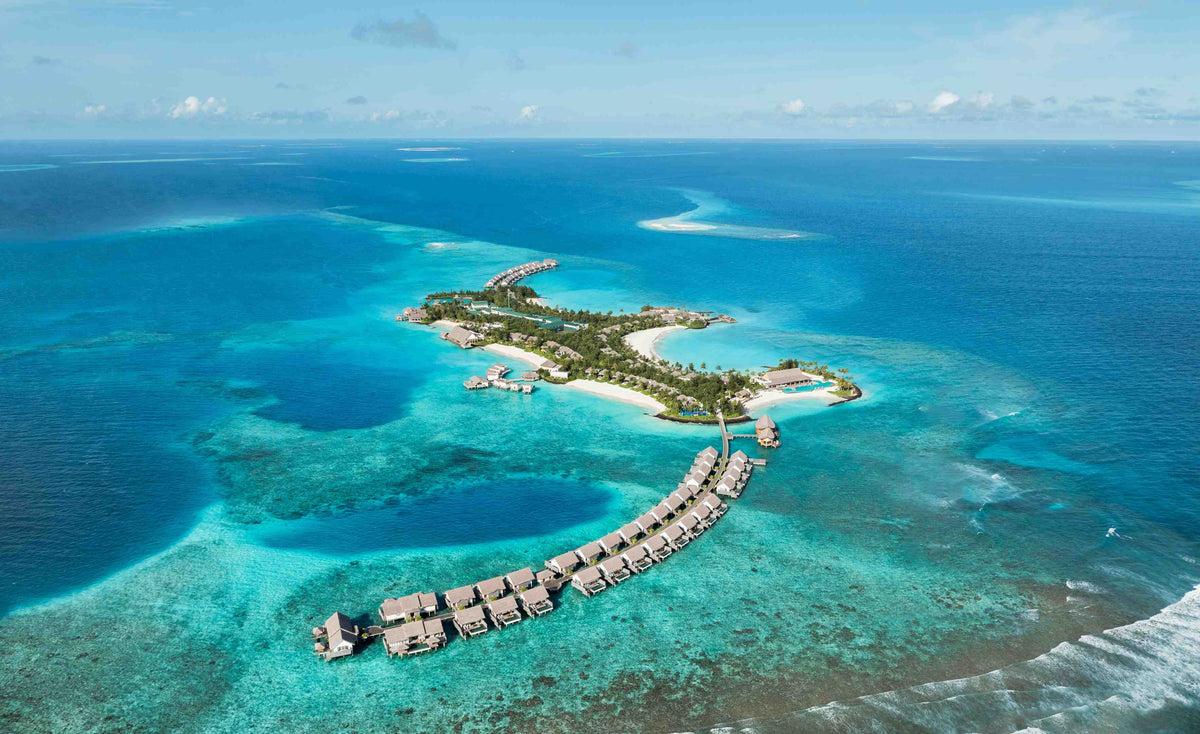 Hilton Maldives Amingiri Resort & Spa from the air, the island in deep blue water with overwater villas along its jetty