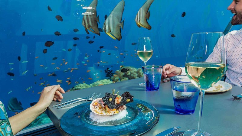 Guests eating at 5.8 Undersea Restaurant at Hurawalhi Maldives as batfish swim past the glass