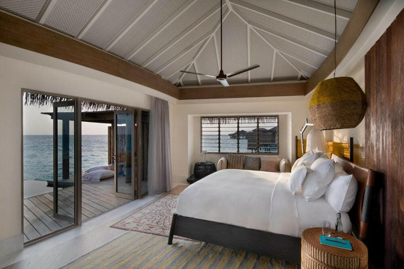 A villa bedroom at InterContinental Maamunagau, rattan pendant light and doors onto the ocean deck.