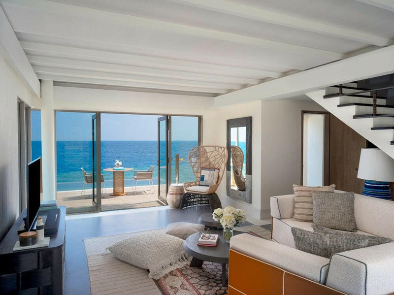 A two-storey villa lounge at InterContinental Maamunagau, staircase behind sofas facing deep blue sea.