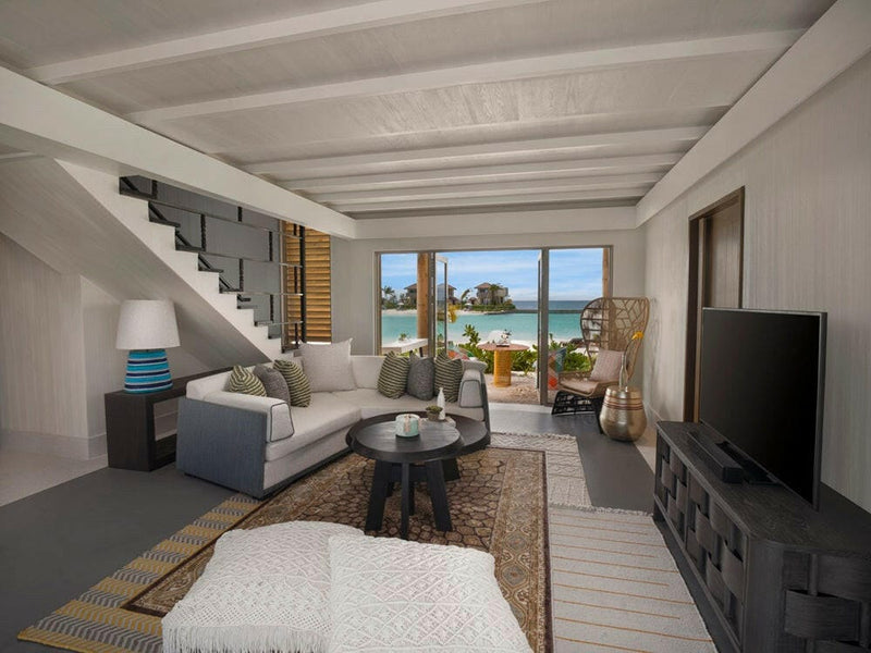 A villa living area at InterContinental Maamunagau, grey sofa below a staircase, garden through the doors.