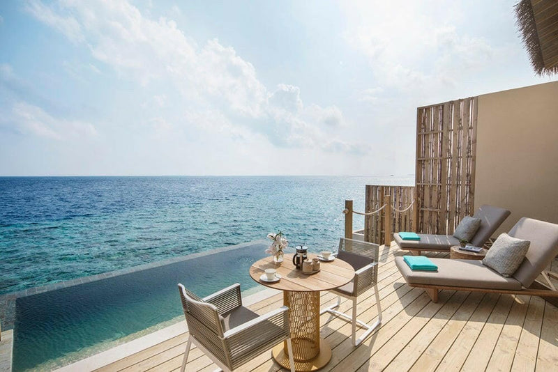 A villa deck at InterContinental Maamunagau, pool edge meeting deep blue water, loungers and a table.