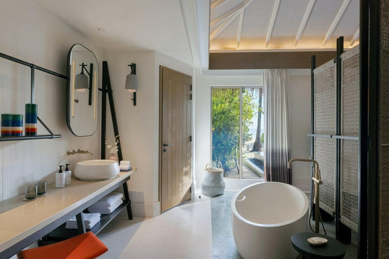 A villa bathroom at InterContinental Maamunagau, twin basins, oval mirrors and a tub by the garden door.