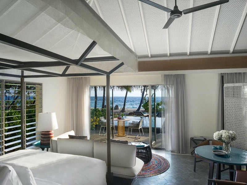 A bedroom at InterContinental Maamunagau with louvred windows and doors onto a terrace and the sea.