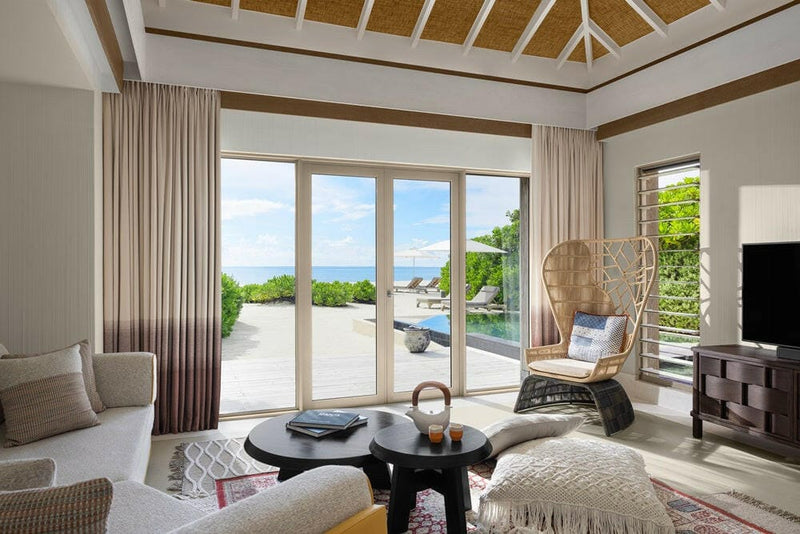 A villa lounge at InterContinental Maamunagau, hanging rattan chair and doors onto a sunlit pool terrace.