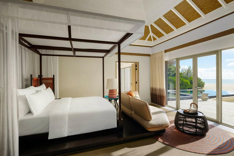 A bedroom at InterContinental Maamunagau, chaise at the foot of the bed and a pool deck outside.