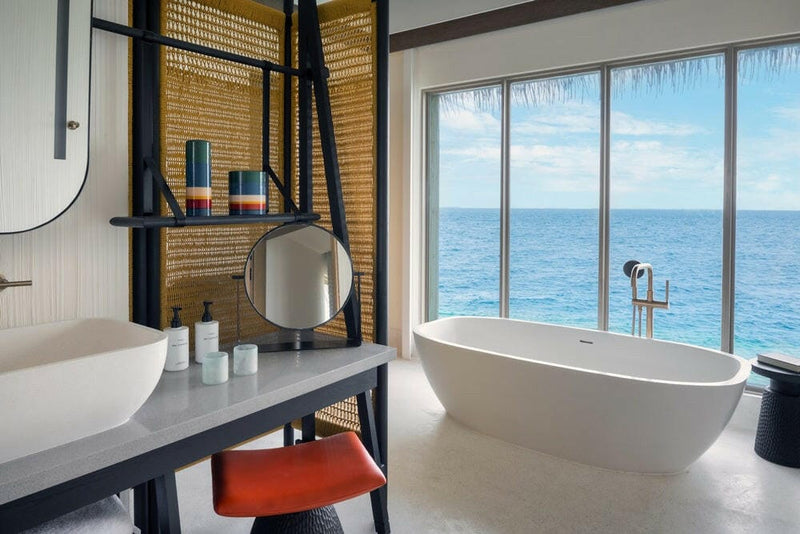 A villa bathroom at InterContinental Maamunagau, oval tub at a window looking out over open sea.
