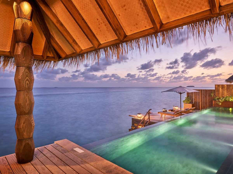 The outdoor deck of a Luxury Sunset Water Villa with Pool at JOALI Maldives at dusk.