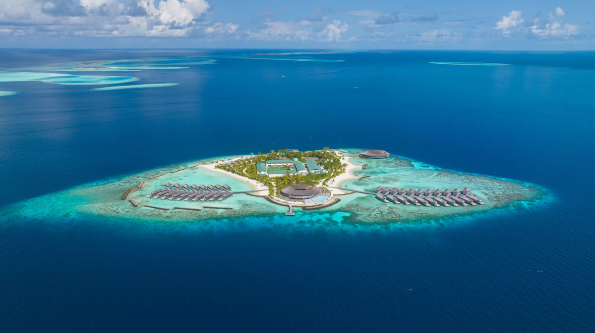 Kagi Maldives Resort & Spa from the air, a small island in deep water with overwater villas on either side