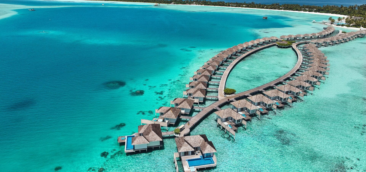 Kandima Maldives from the air, a long loop of overwater villas over turquoise shallows