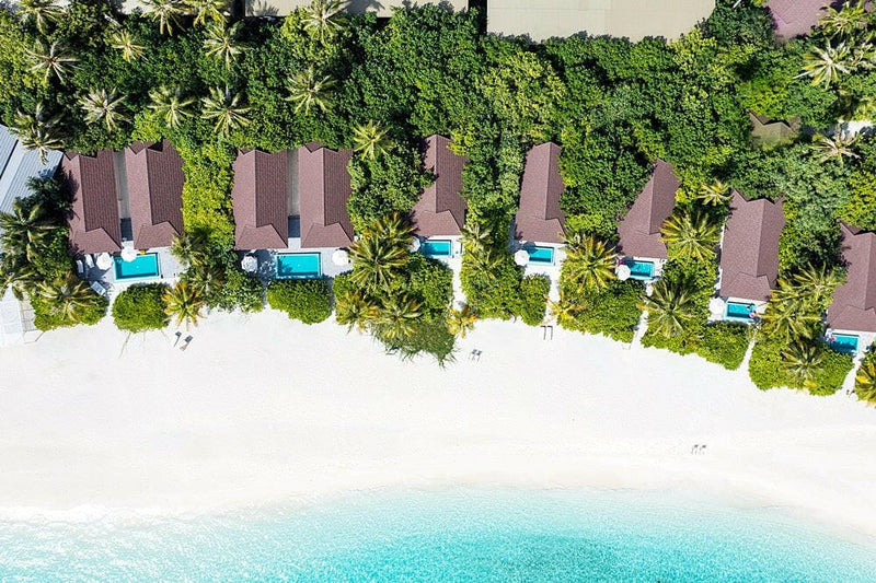 Beach villas at The Standard Huruvalhi from above, a curved row of red roofs and pools along the beach.