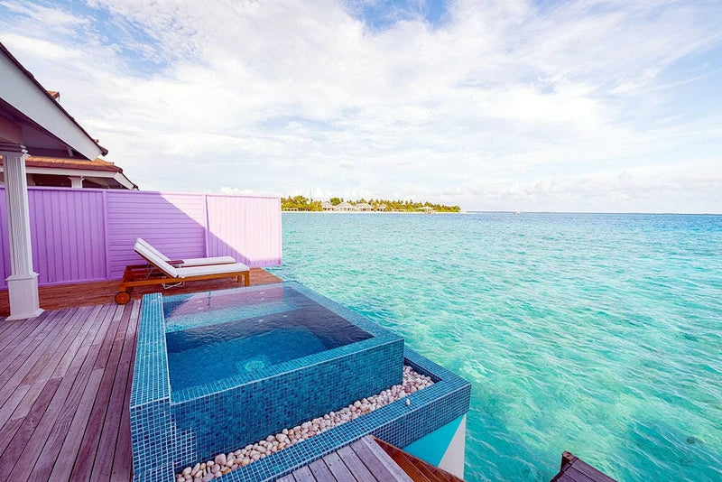 A water villa deck at The Standard Huruvalhi, a blue mosaic plunge pool and lounger facing the lagoon.