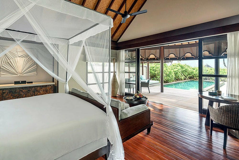 A villa bedroom at Four Seasons Kuda Huraa, a four poster bed under netting with the pool outside