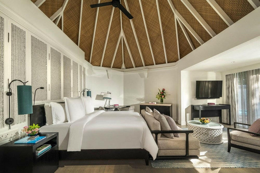 A villa bedroom at Four Seasons Kuda Huraa, a white bed and two armchairs under a high thatched ceiling
