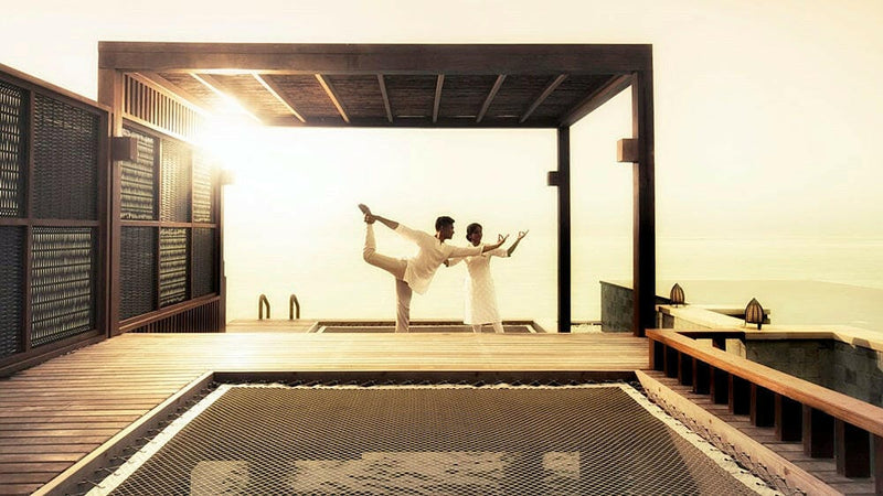 Two guests practising yoga on an overwater deck at Four Seasons Kuda Huraa at sunrise