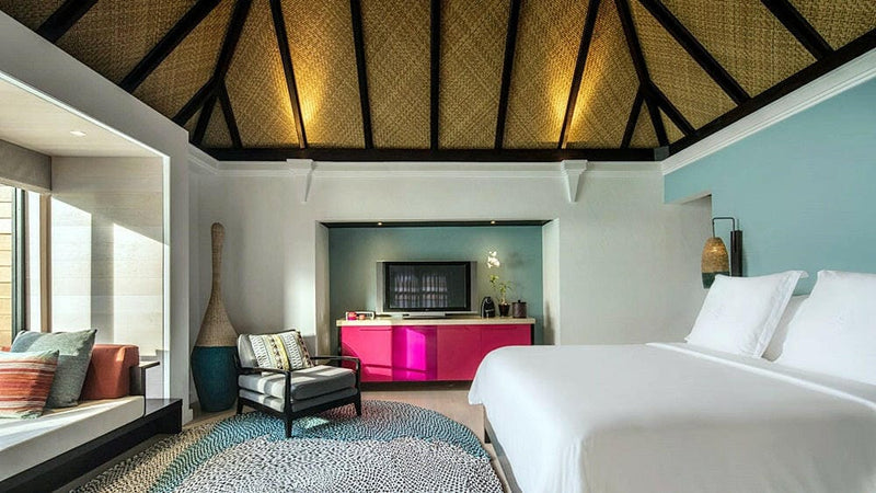 A villa bedroom at Four Seasons Kuda Huraa, a bright magenta panel behind the bed above a patterned rug