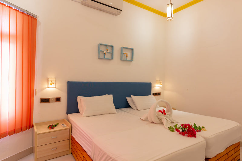 Room at Dream Inn Thulusdhoo with two single beds pushed together under a blue headboard, orange window blinds and a bedside table