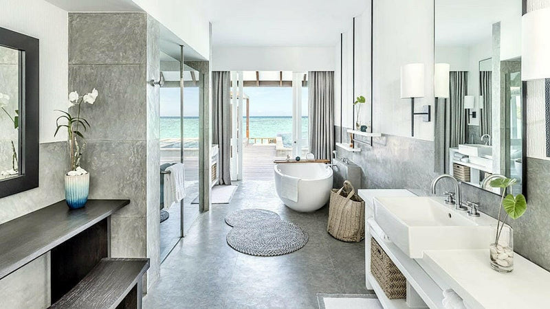 A villa bathroom at Four Seasons Landaa Giraavaru, orchids on a stone console beside a freestanding tub