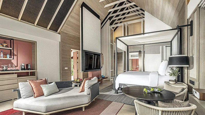 A suite at Four Seasons Landaa Giraavaru, a long sofa and a four poster bed under a high pitched roof