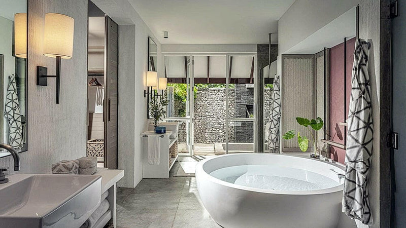 A villa bathroom at Four Seasons Landaa Giraavaru, an oval freestanding tub against a patterned wall