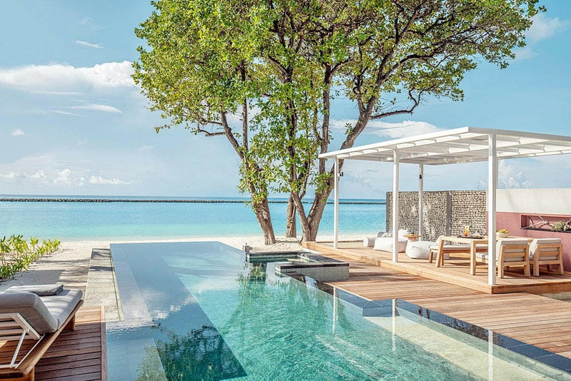 A villa terrace at Four Seasons Landaa Giraavaru, an infinity pool and a shaded daybed facing the beach