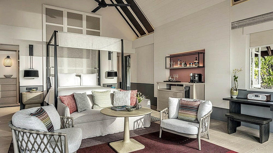 A villa bedroom at Four Seasons Landaa Giraavaru, a four poster bed with a sofa and writing desk