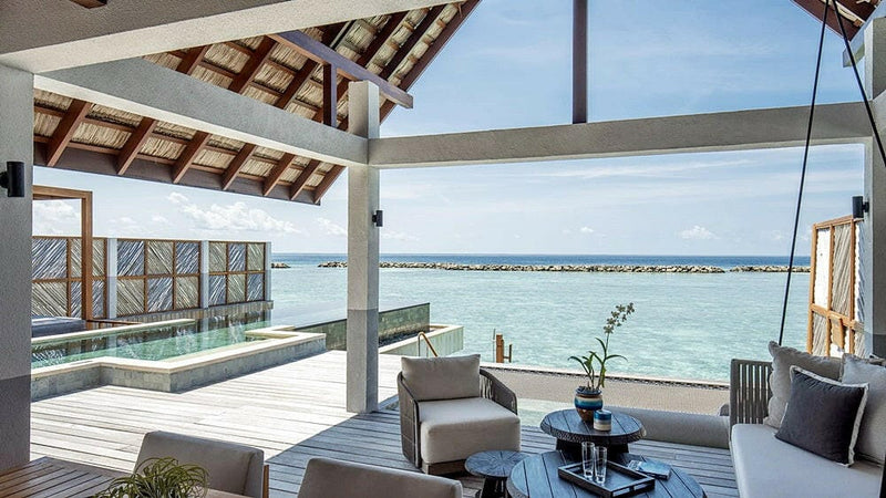 An overwater deck at Four Seasons Landaa Giraavaru, armchairs and a low table beside the pool