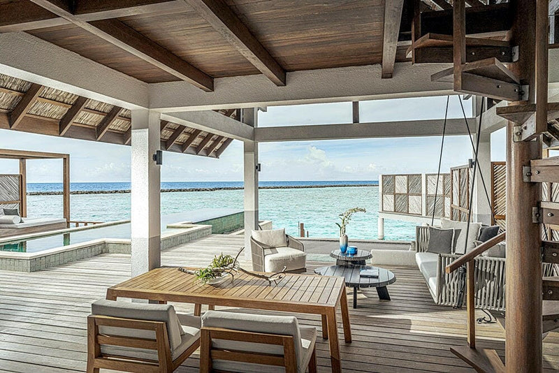 A shaded deck at Four Seasons Landaa Giraavaru, a dining table and seating under a timber roof over the water