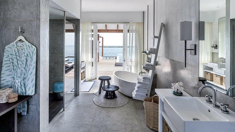 A villa bathroom at Four Seasons Landaa Giraavaru, a freestanding tub and twin basins with a robe by the door to the sea