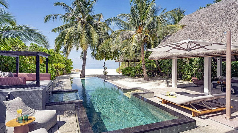 A beach villa at Four Seasons Landaa Giraavaru, a thatched pavilion and private pool among the palms