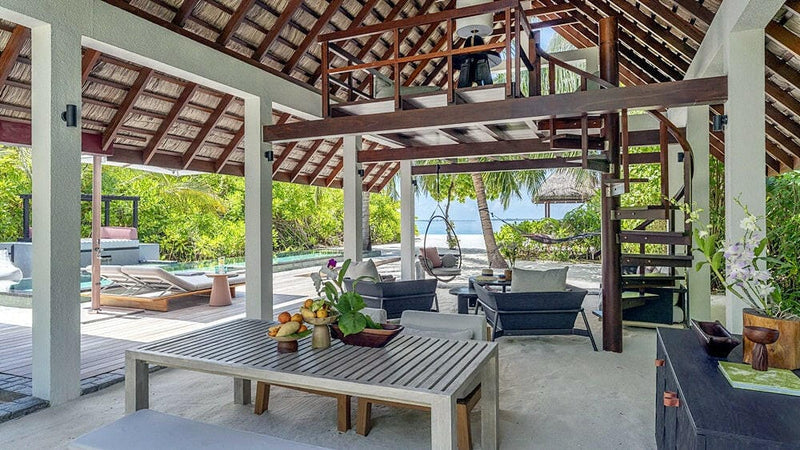An open dining pavilion at Four Seasons Landaa Giraavaru, a long table under a thatched roof facing the beach