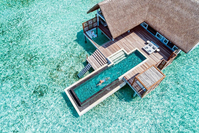 A water villa at Four Seasons Landaa Giraavaru from directly above, its long pool and deck over turquoise shallows