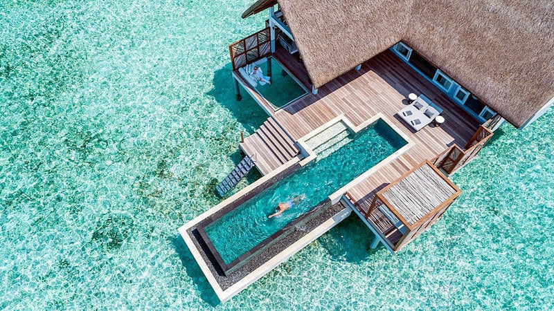 A water villa at Four Seasons Landaa Giraavaru from directly above, its long pool and deck over turquoise shallows