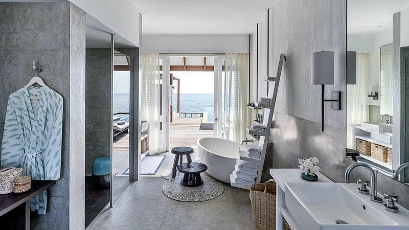 A villa bathroom at Four Seasons Landaa Giraavaru, a freestanding tub and twin basins with a robe by the door to the sea