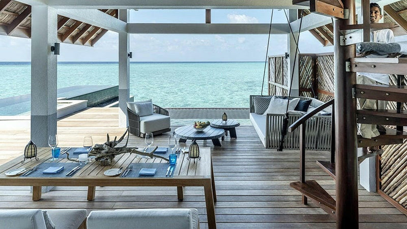 The deck of a water villa at Four Seasons Landaa Giraavaru, a dining table laid beside a hanging chair