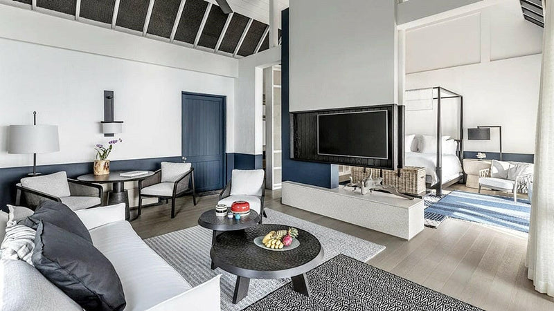 The living room of a water villa at Four Seasons Landaa Giraavaru, sofa and dining table with the lagoon through the glass