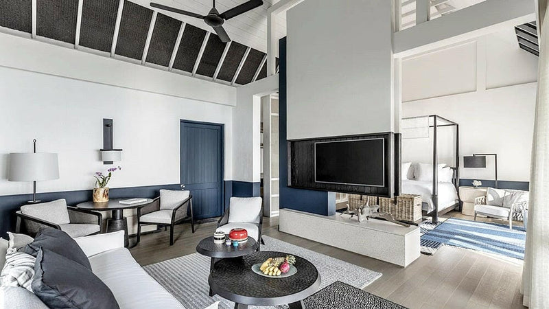 The living room of a water villa at Four Seasons Landaa Giraavaru, sofa and dining table with the lagoon through the glass
