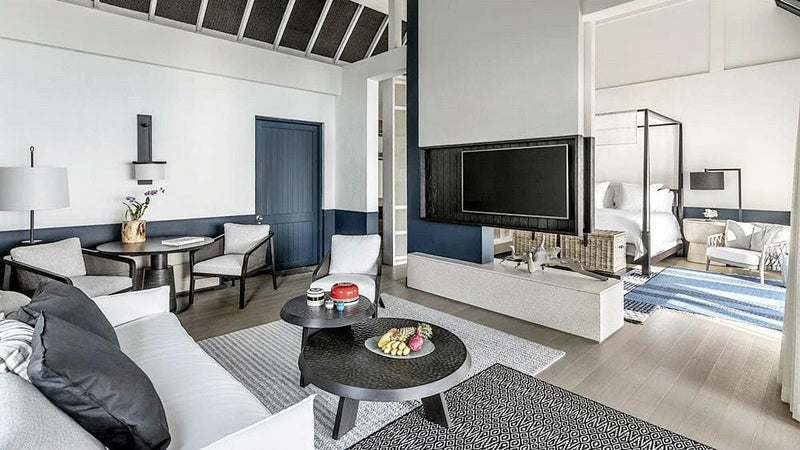 The living room of a water villa at Four Seasons Landaa Giraavaru, sofa and dining table with the lagoon through the glass