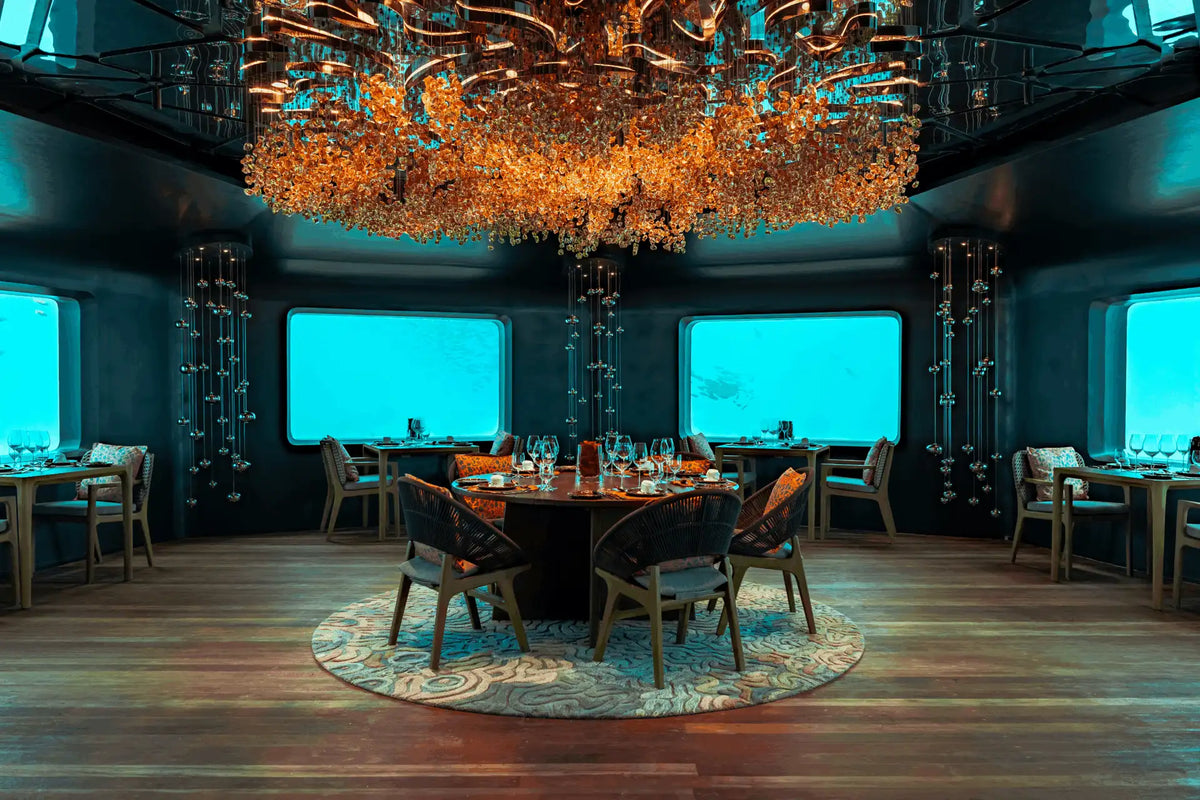 The dining room of BUBBLE at Meyyafushi Maldives, wide windows on to the lagoon under a chandelier of orange coral shapes