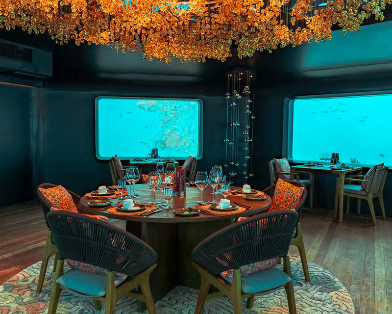 A table laid for dinner beneath a window in BUBBLE at Meyyafushi Maldives