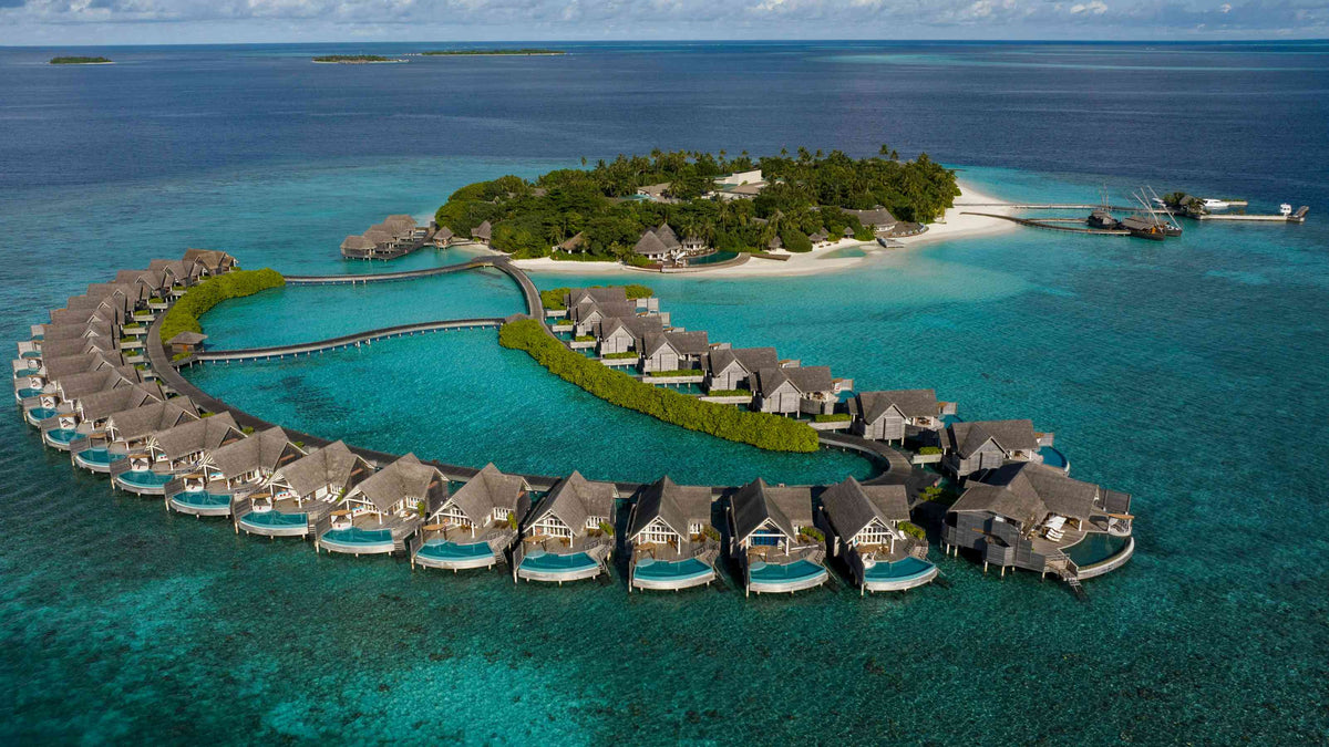 Milaidhoo Maldives from the air, the overwater villas curving round the lagoon off a green island