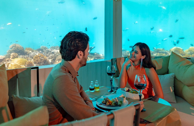 A couple at dinner in M6m at OZEN LIFE Maadhoo, the coral reef behind the glass