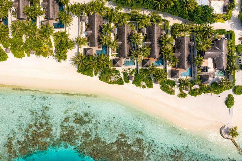 The beach at OZEN RESERVE Bolifushi from the air, villas and pools behind the palms along the sand