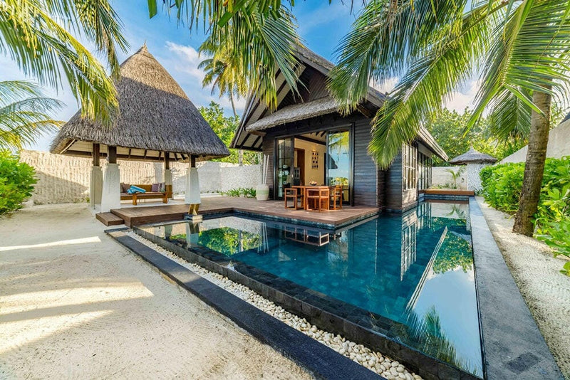 A beach villa at OZEN RESERVE Bolifushi, a long dark tiled pool running beside the thatched pavilion