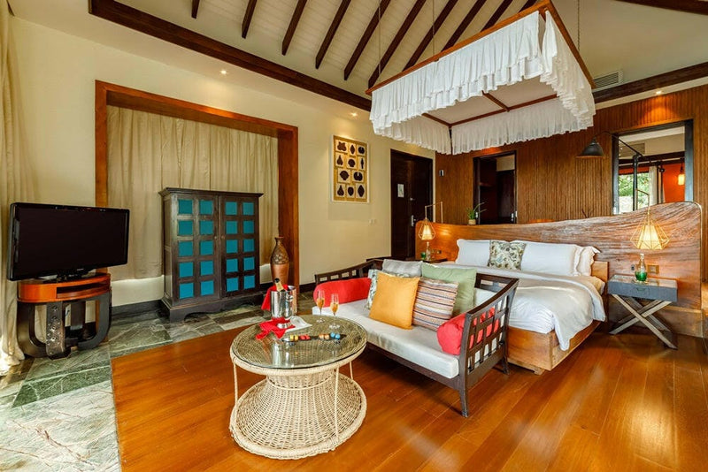 A villa bedroom at OZEN RESERVE Bolifushi, orange and red cushions on the bench at the foot of the bed